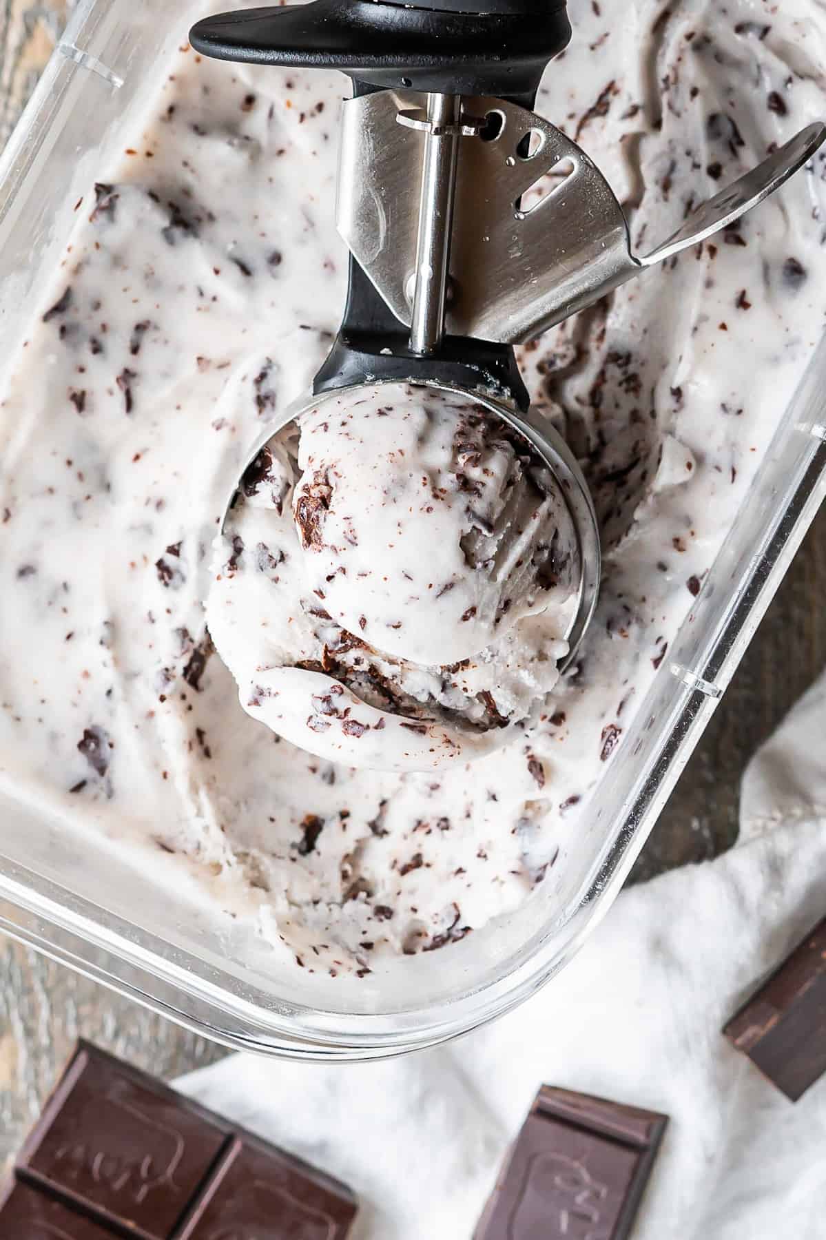 An ice cream scoop of stracciatella vegan gelato resting in the gelato container.