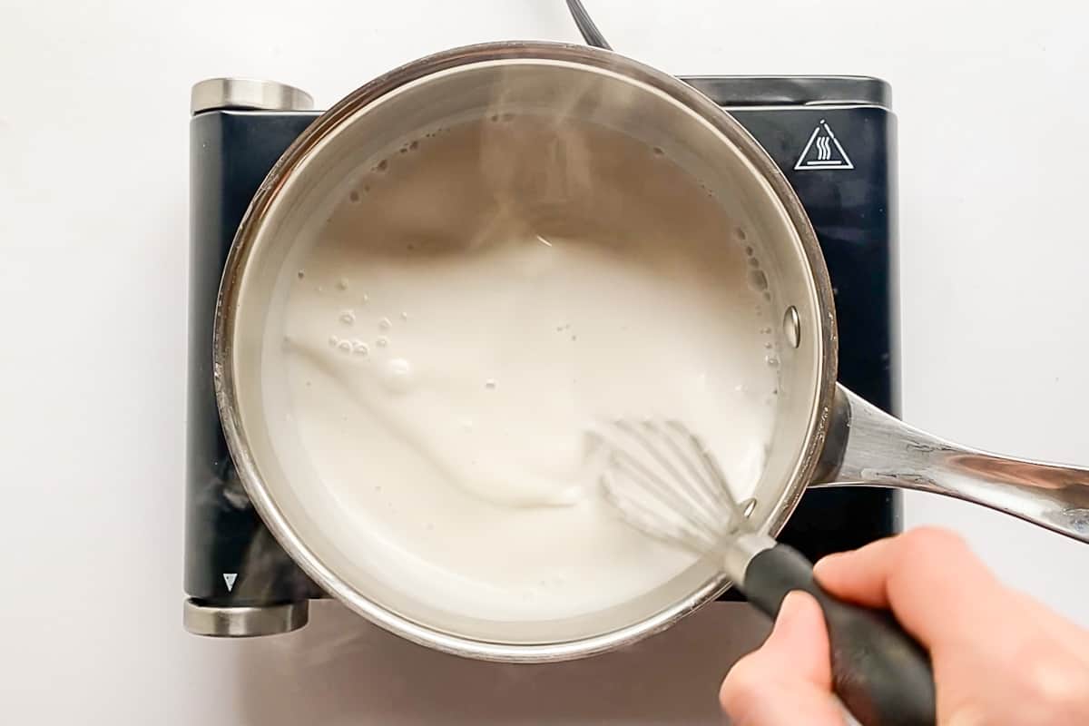 Whisking together a coconut milk and sugar mixture in a small pot on a burner.