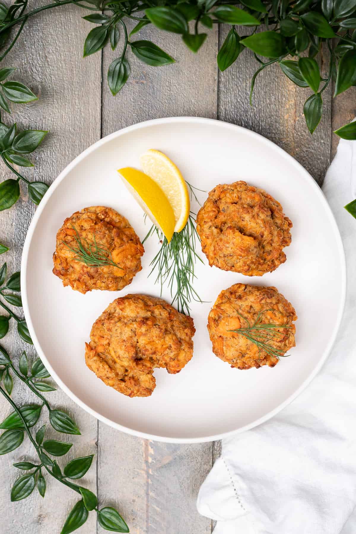 Four baked salmon cakes on a plate garnished with fresh dill and lemon.