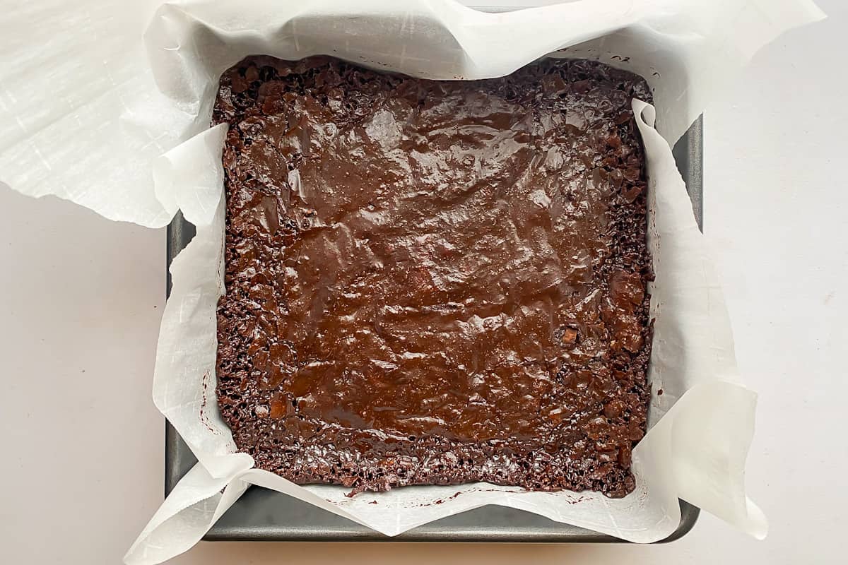 The baked healthy almond flour brownies with a shiny top cooling in the brownie pan.