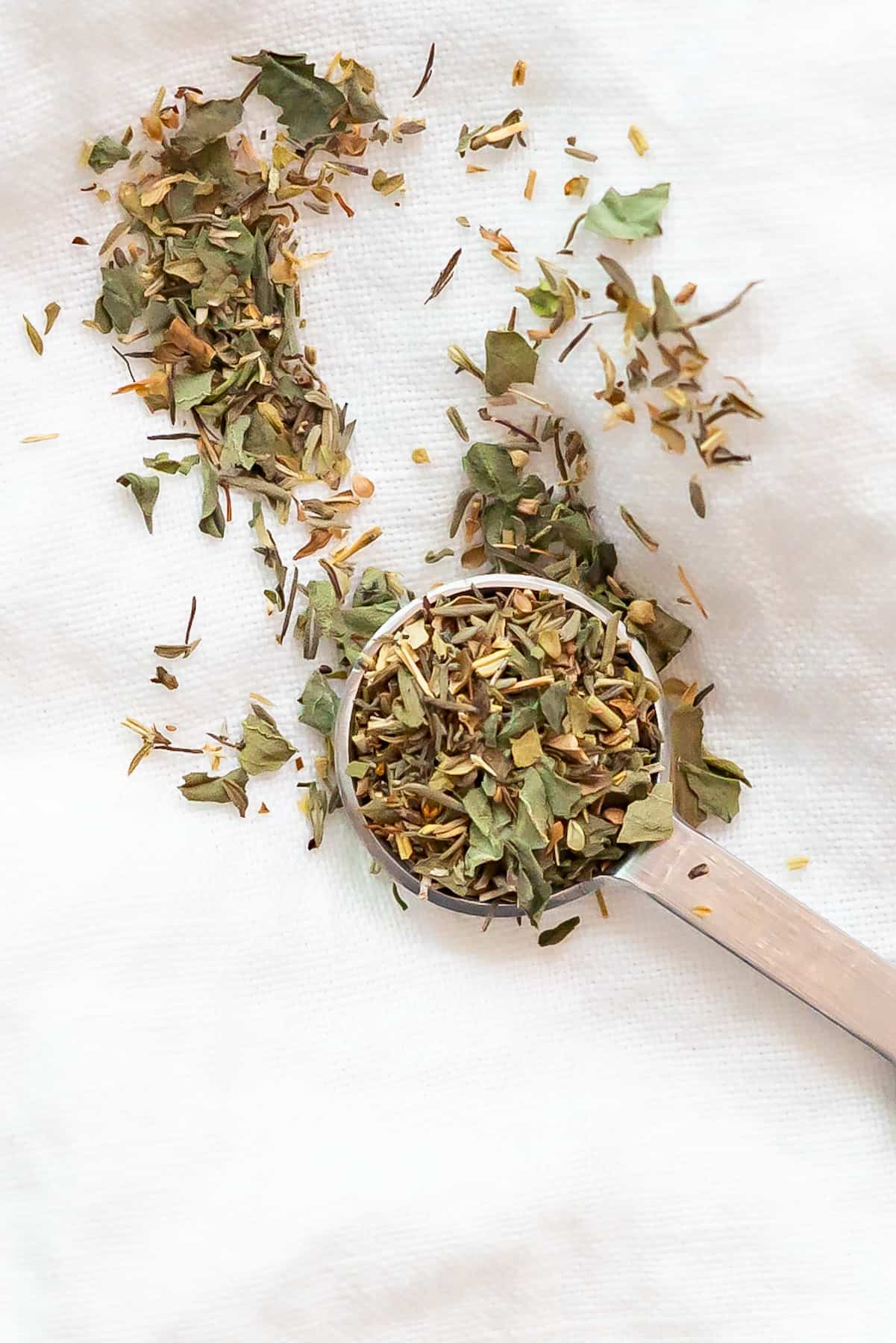 A teaspoon with an Italian seasoning substitute made of basil, oregano, rosemary, and thyme.