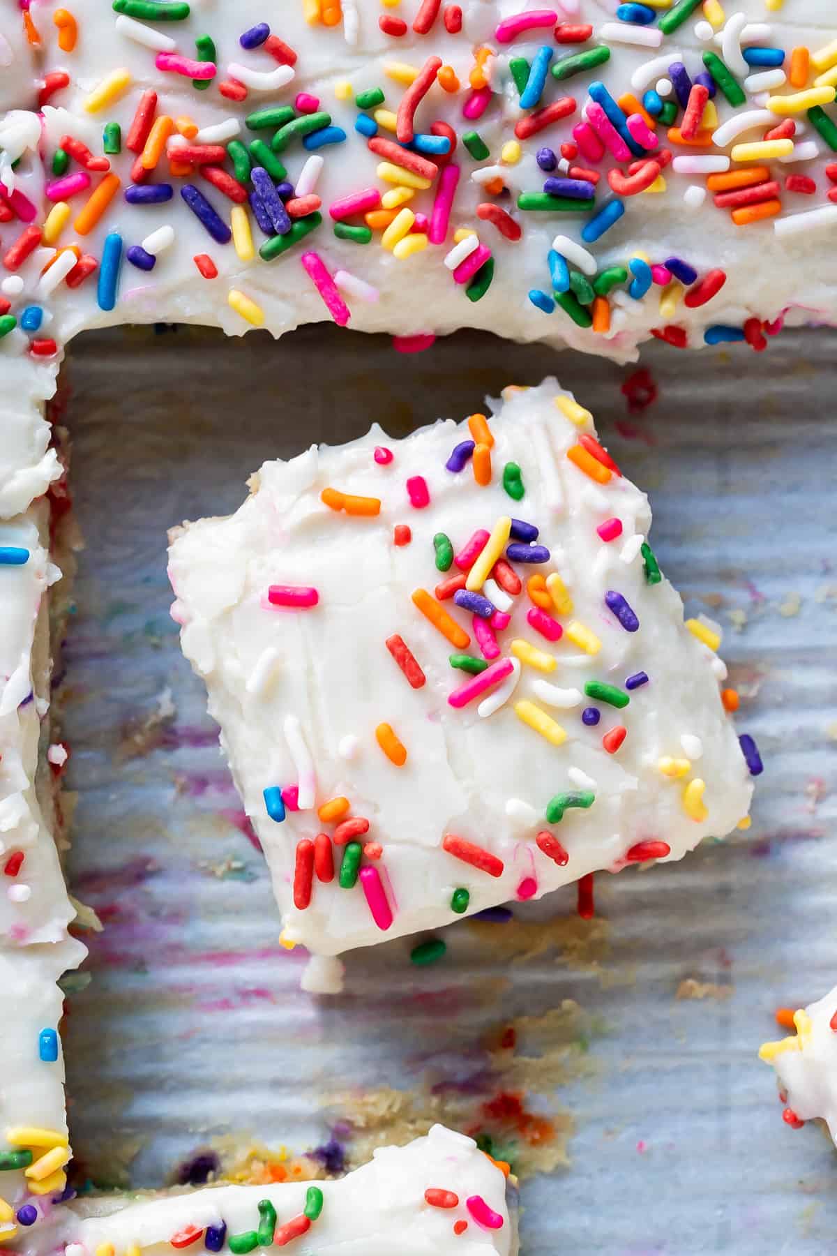 A square piece of vegan and gluten-free cake with rainbow sprinkles and a smooth vegan 'cream cheese' frosting.