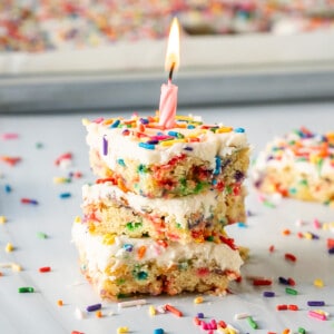 A stack of three pieces of vegan gluten free funfetti birthday cake with a pink birthday candle.