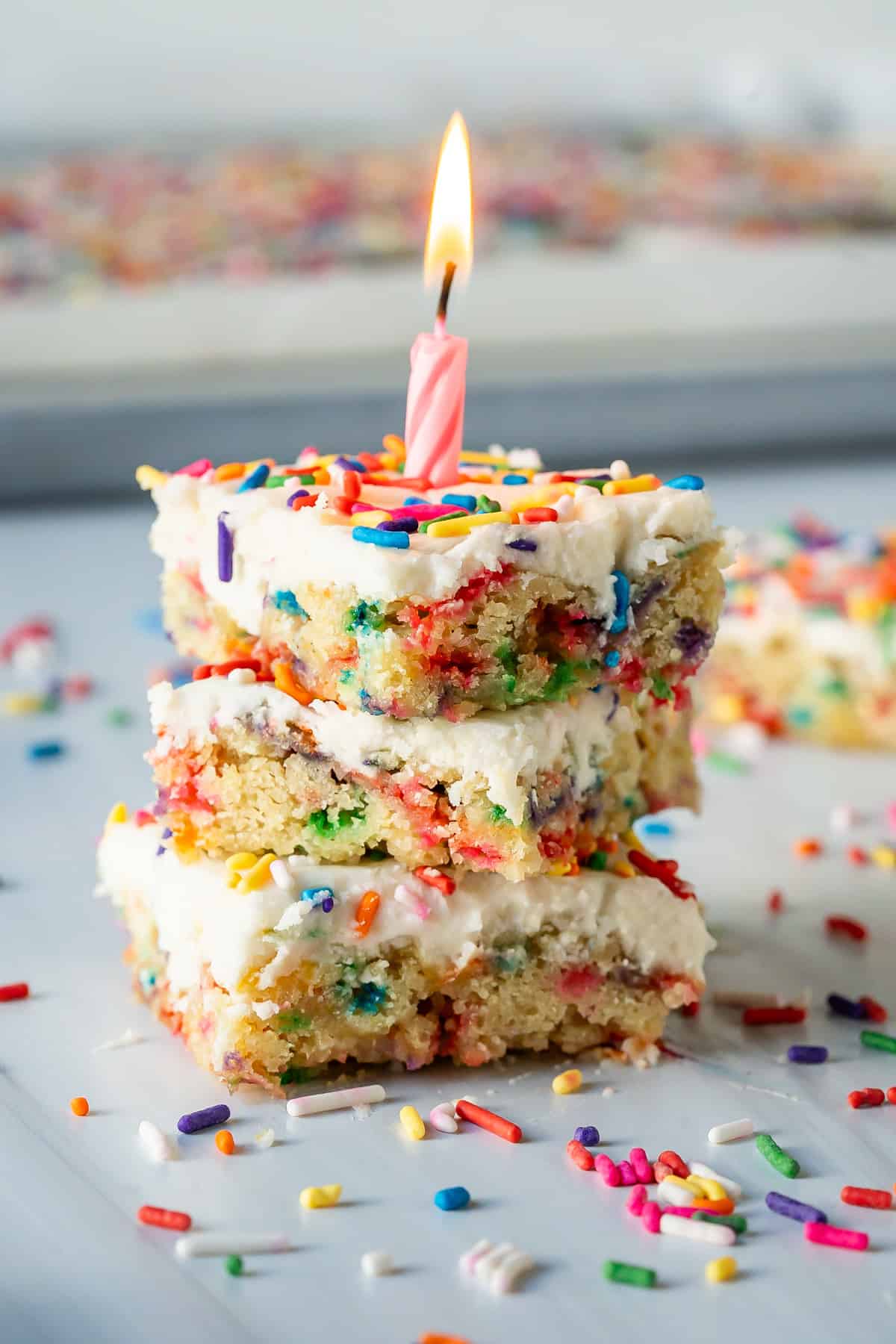 A stack of three pieces of vegan gluten free funfetti birthday cake with a pink birthday candle.