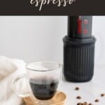 Aeropress espresso in a clear espresso mug with an aeropress and espresso beans.