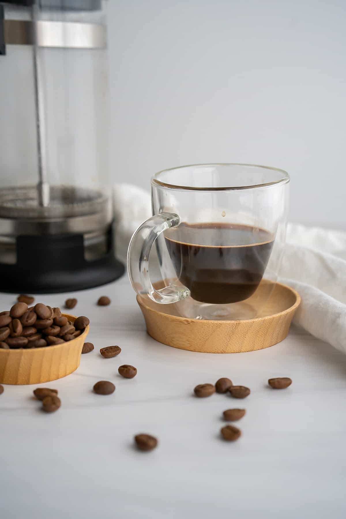 A double shot of french press espresso in a clear glass espresso cup with the french press beside it.