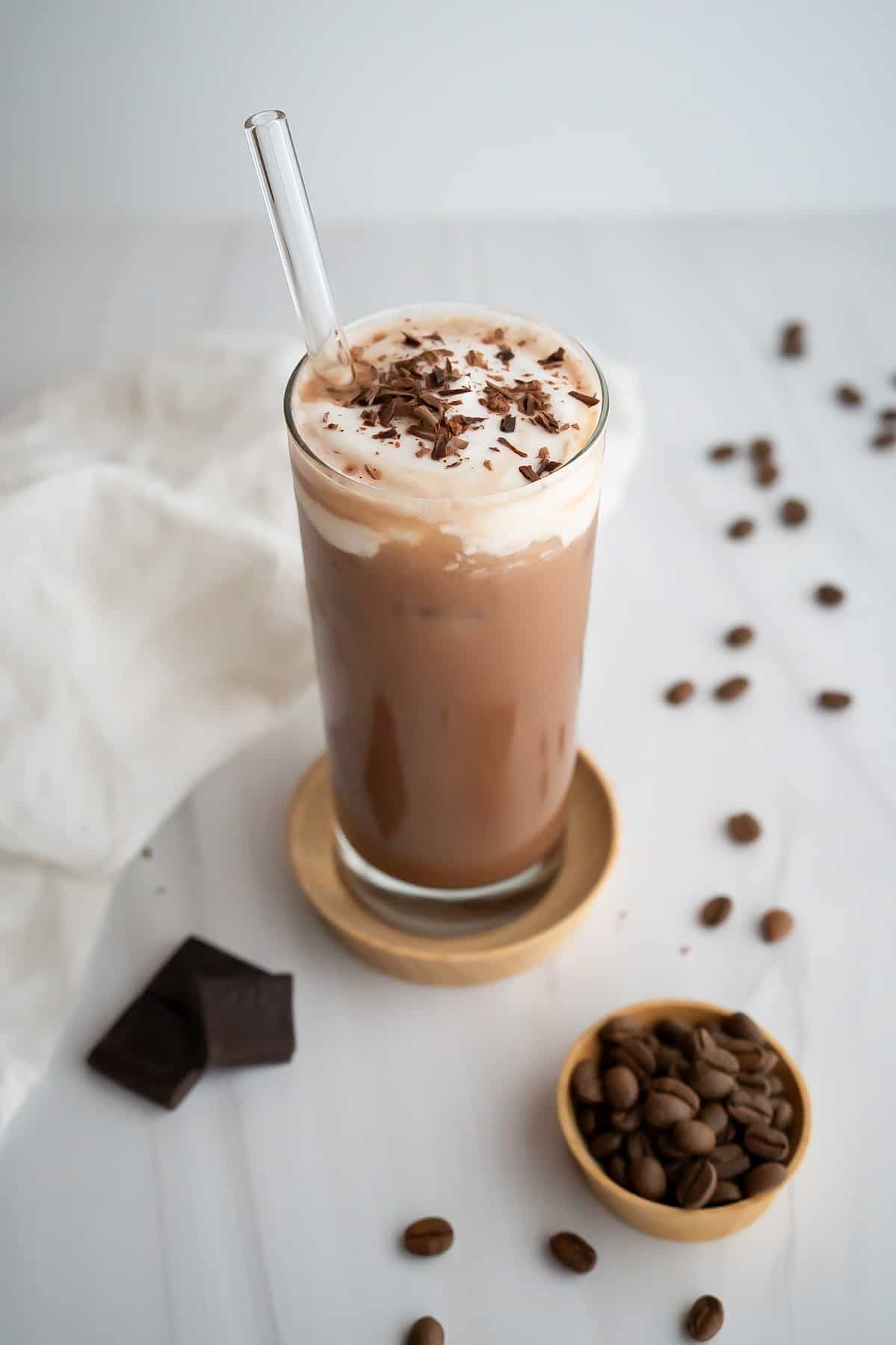 A tall glass with an iced mocha topped with whipped cream and chocolate shavings.
