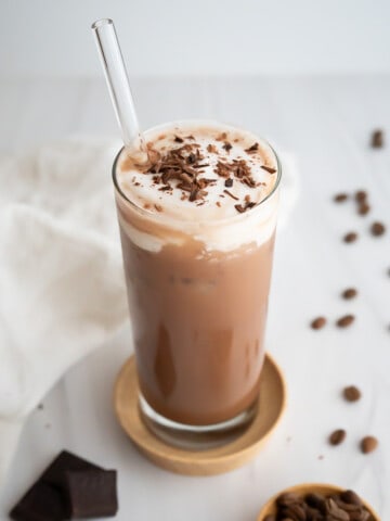A tall glass with an iced mocha topped with whipped cream and chocolate shavings.