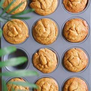 A muffin tin filled with cooling healthy pumpkin muffins with golden tops.