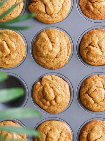 A muffin tin filled with cooling healthy pumpkin muffins with golden tops.