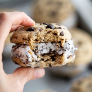 A close up of an ice cream cookie sandwich with a bite taken out of it to show the layers of chocolate chip cookies and ice cream.