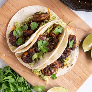 Three blackened shrimp tacos topped with cilantro leaves and flaky sea salt.