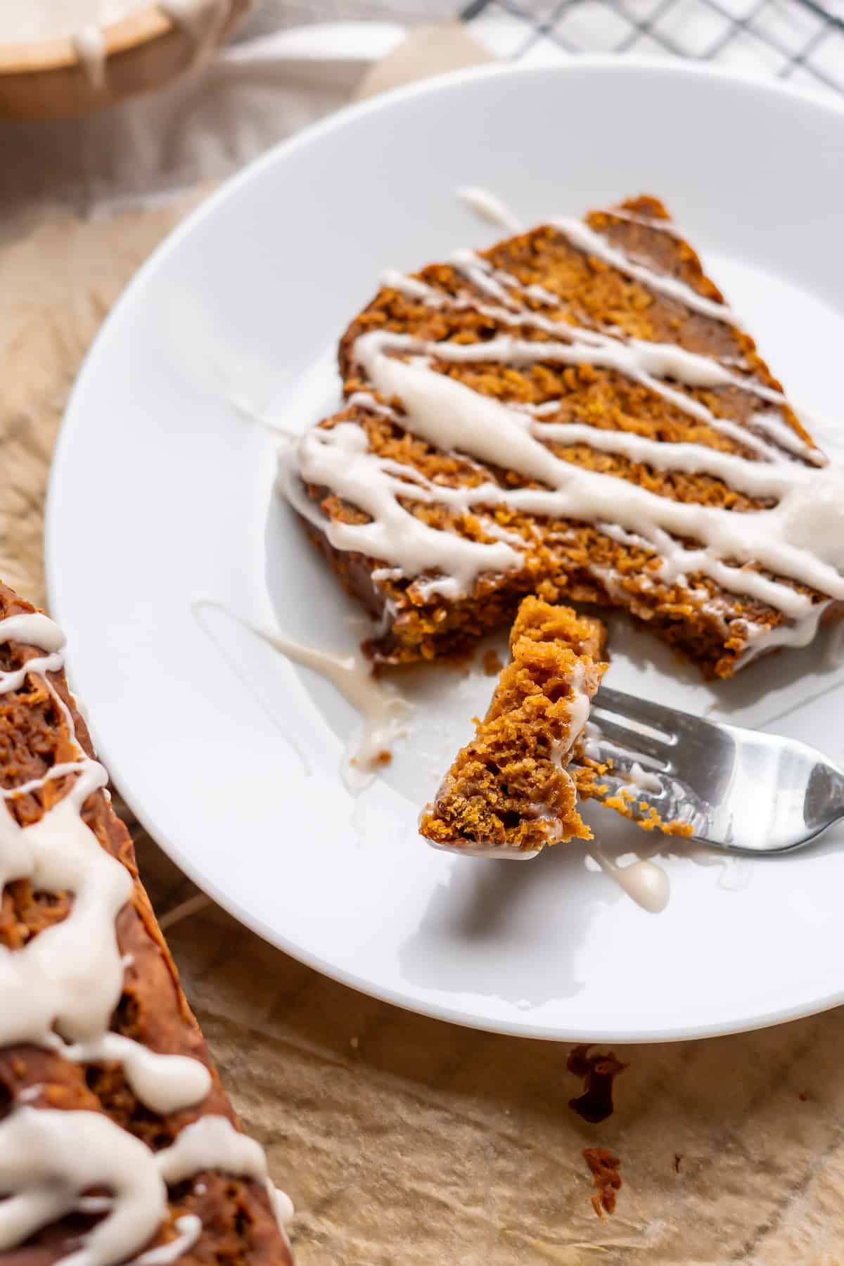 A bite of gluten-free pumpkin bread on a fork beside a slice drizzled with icing.