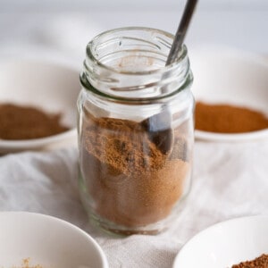 A small jar of homemade pumpkin pie spice surrounded by the four individual spices that compose it.
