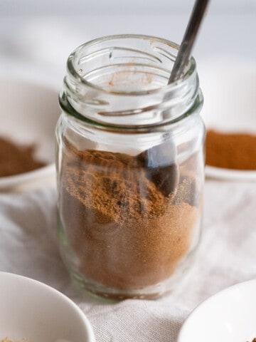 A small jar of homemade pumpkin pie spice surrounded by the four individual spices that compose it.