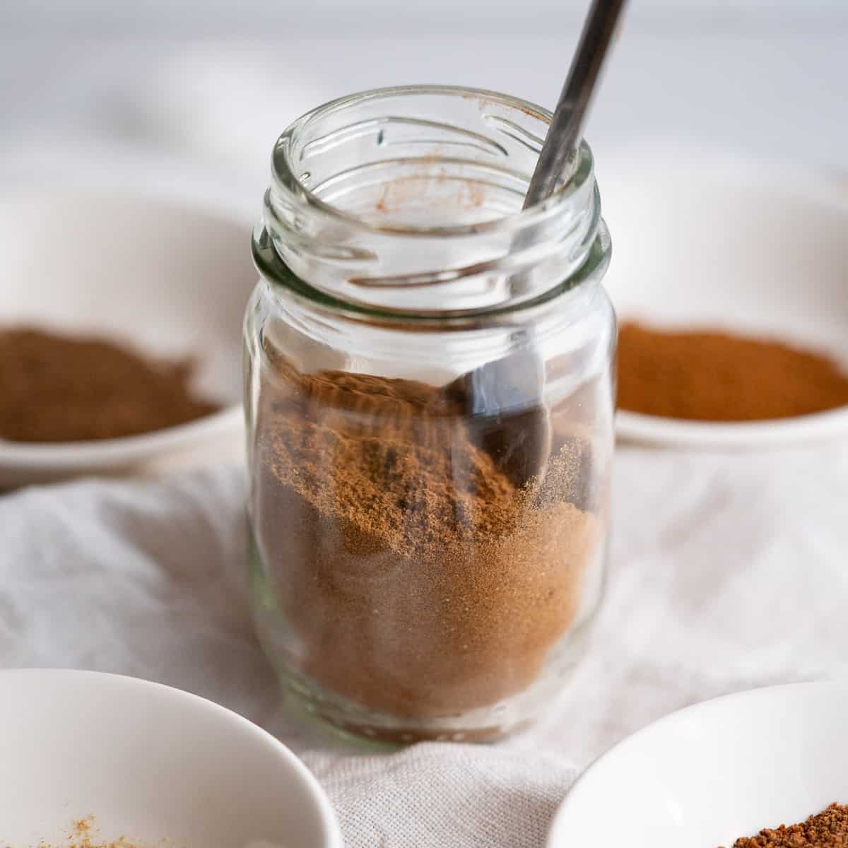 A small jar of homemade pumpkin pie spice surrounded by the four individual spices that compose it.
