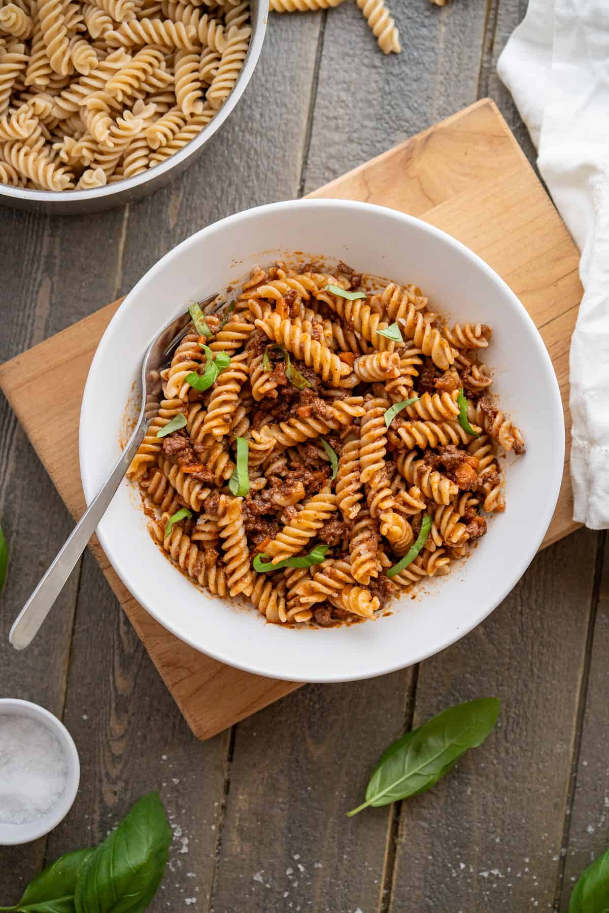 A bowl of lamb ragu with fusilli pasta served with basil leaves as a garnish.