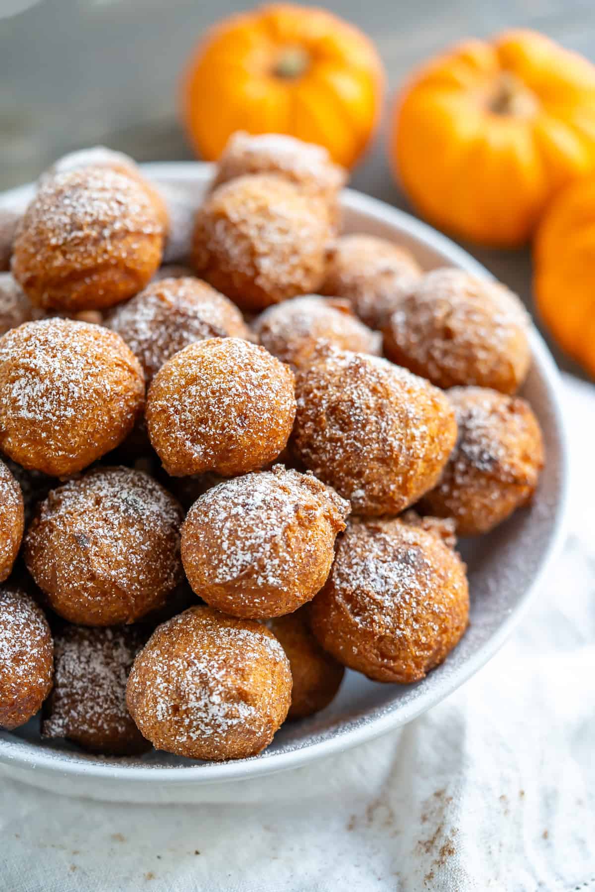 A bowl filled with gluten free pumpkin donut holes dusted with powdered sugar.