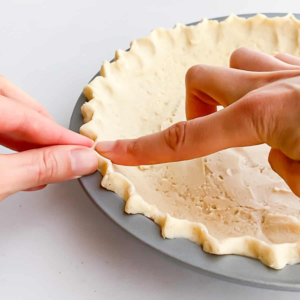 Using two hands to gently crimp a decorative edge along the unbaked pie crust.