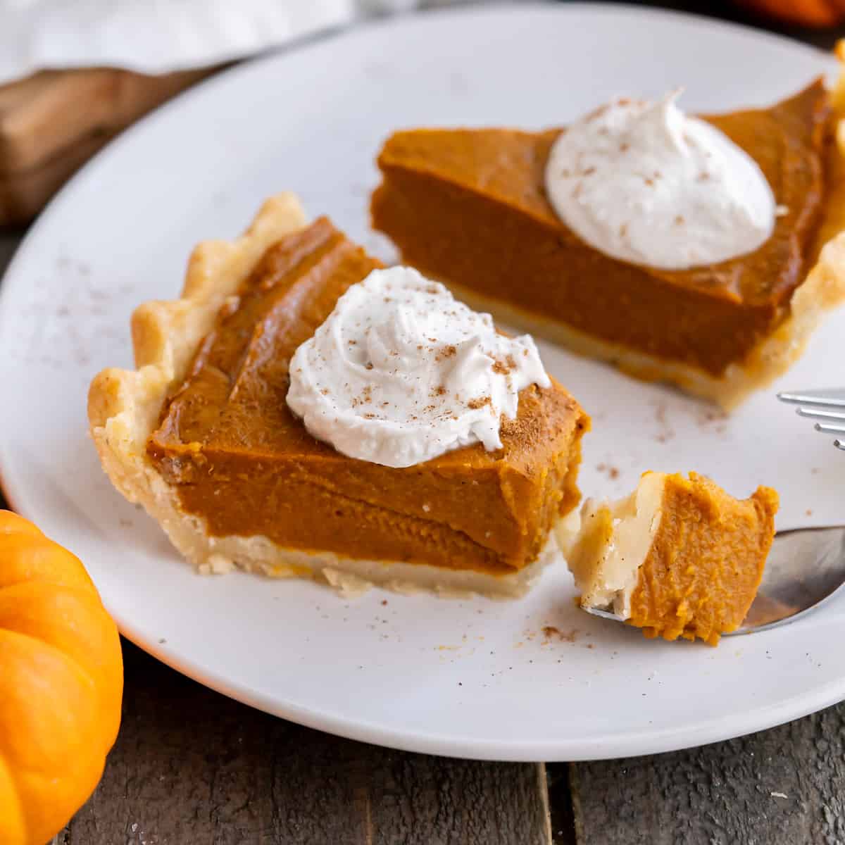 A bite of gluten-free vegan pumpkin pie on a fork beside a slice topped with vegan whipped cream.