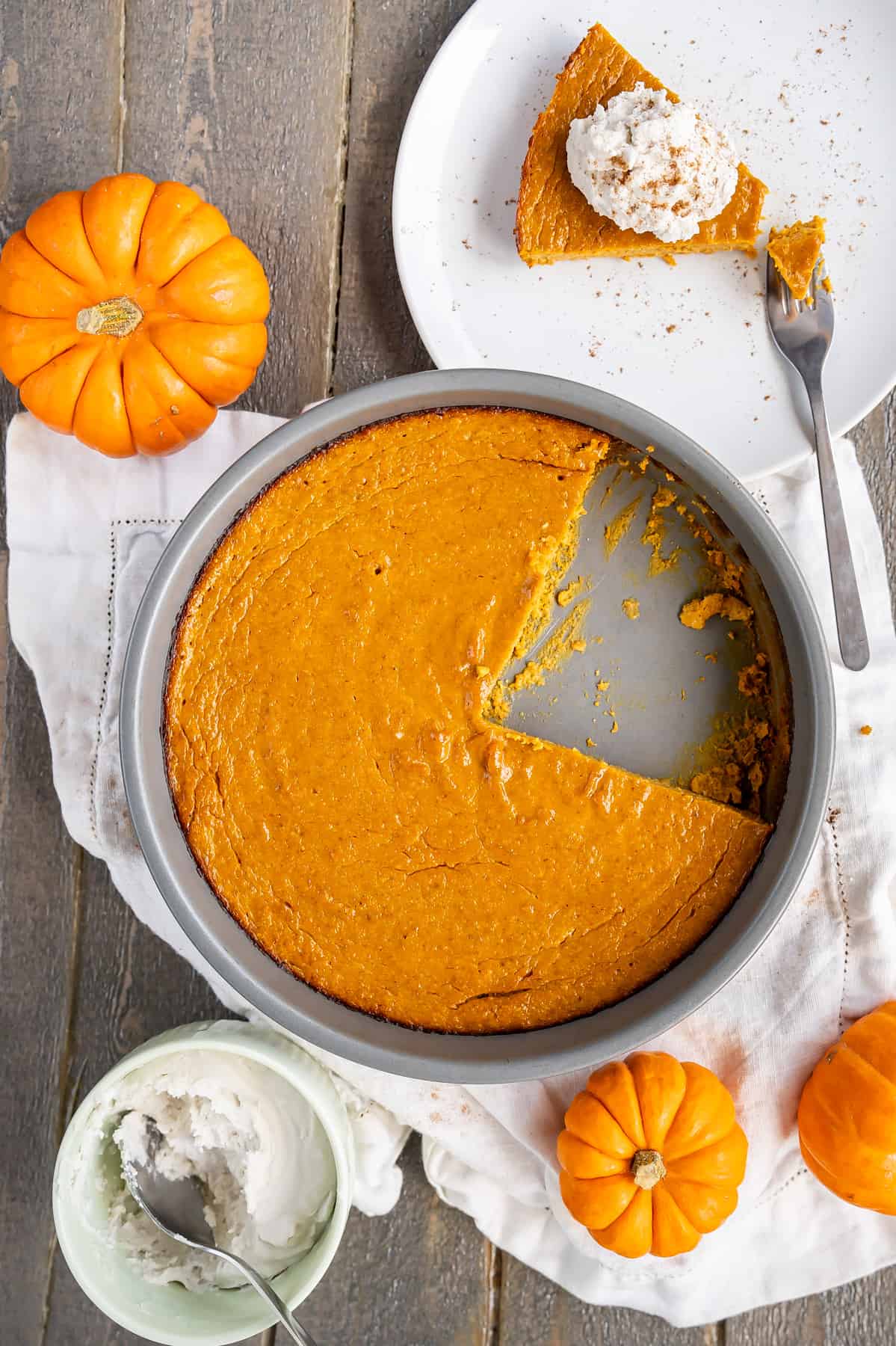 A crustless pumpkin pie surrounded by a slice with whipped cream and mini pumpkins.
