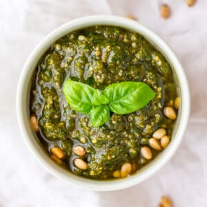A bowl of dairy-free pesto garnished with toasted pine nuts and basil leaves.