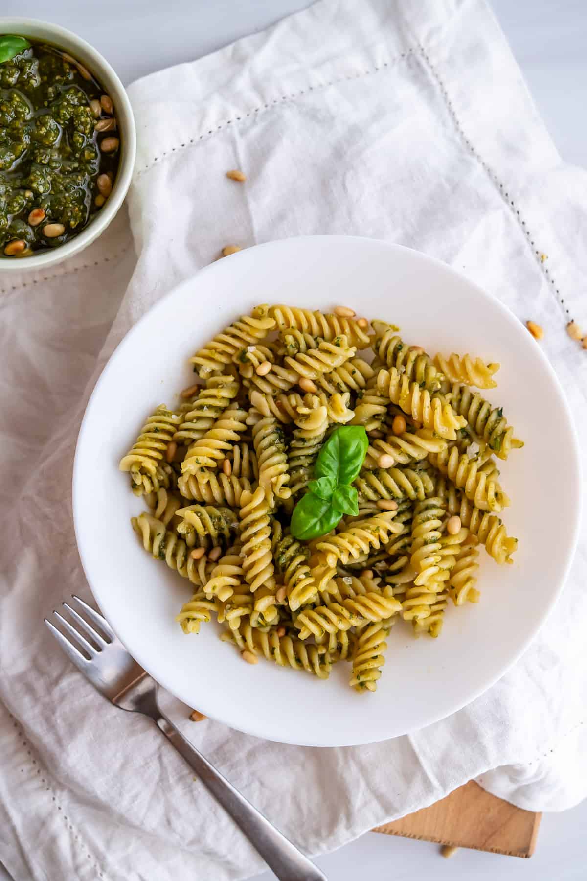 A bowl of pesto pasta garnished with basil leaves and toasted pine nuts.