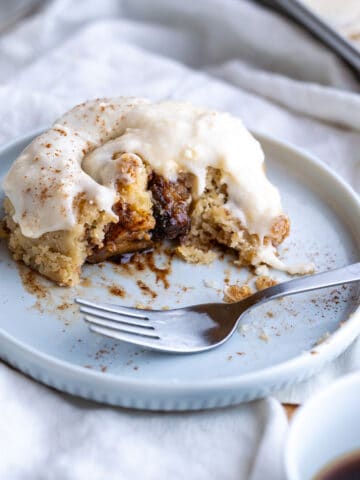 A buttery half-eaten gluten-free cinnamon roll with a gooey cinnamon center and creamy cream cheese frosting!