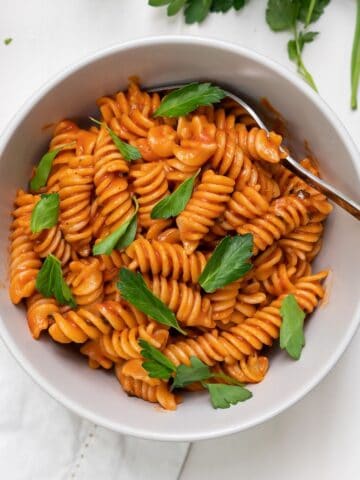 A bowl of dairy-free vodka sauce tossed with pasta and garnished with Italian parsley.