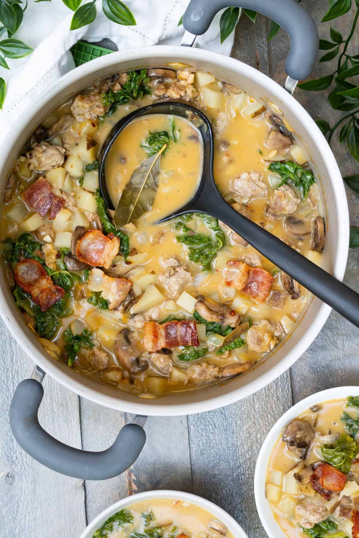 A pot and two serving bowls of healthy zuppa toscana with a savory coconut milk broth.