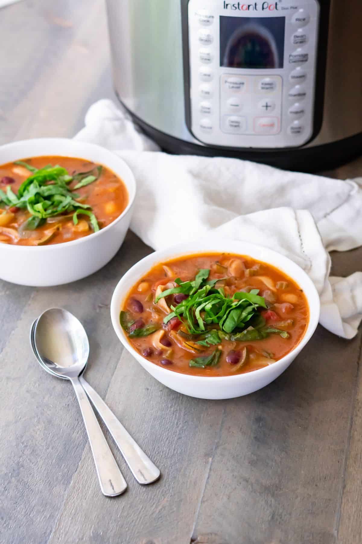 Two bowls of minestrone vegetable soup set in front of an instant pot.