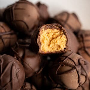 A pile of chocolate covered peanut butter balls with one split open to show the creamy peanut butter center.