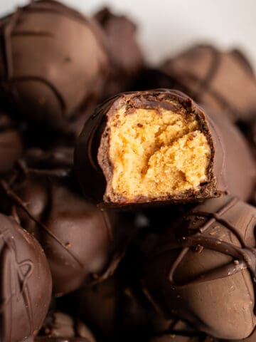 A pile of chocolate covered peanut butter balls with one split open to show the creamy peanut butter center.