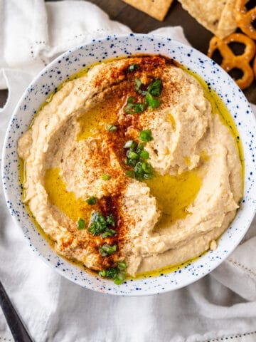 A bowl of homemade chickpea hummus with a sprinkling of paprika and chopped green onions.