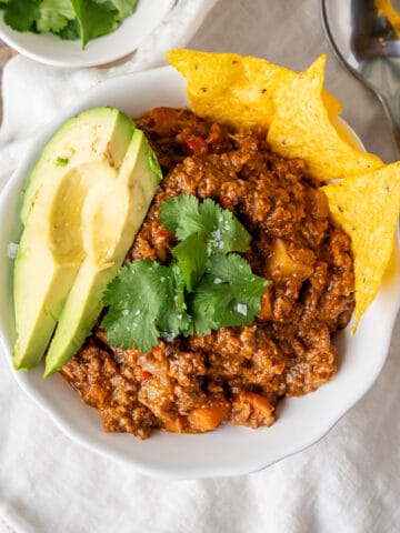 A bowl of healthy no bean chili served with tortilla chips, avocado slices, cilantro leaves, and flaky sea salt.