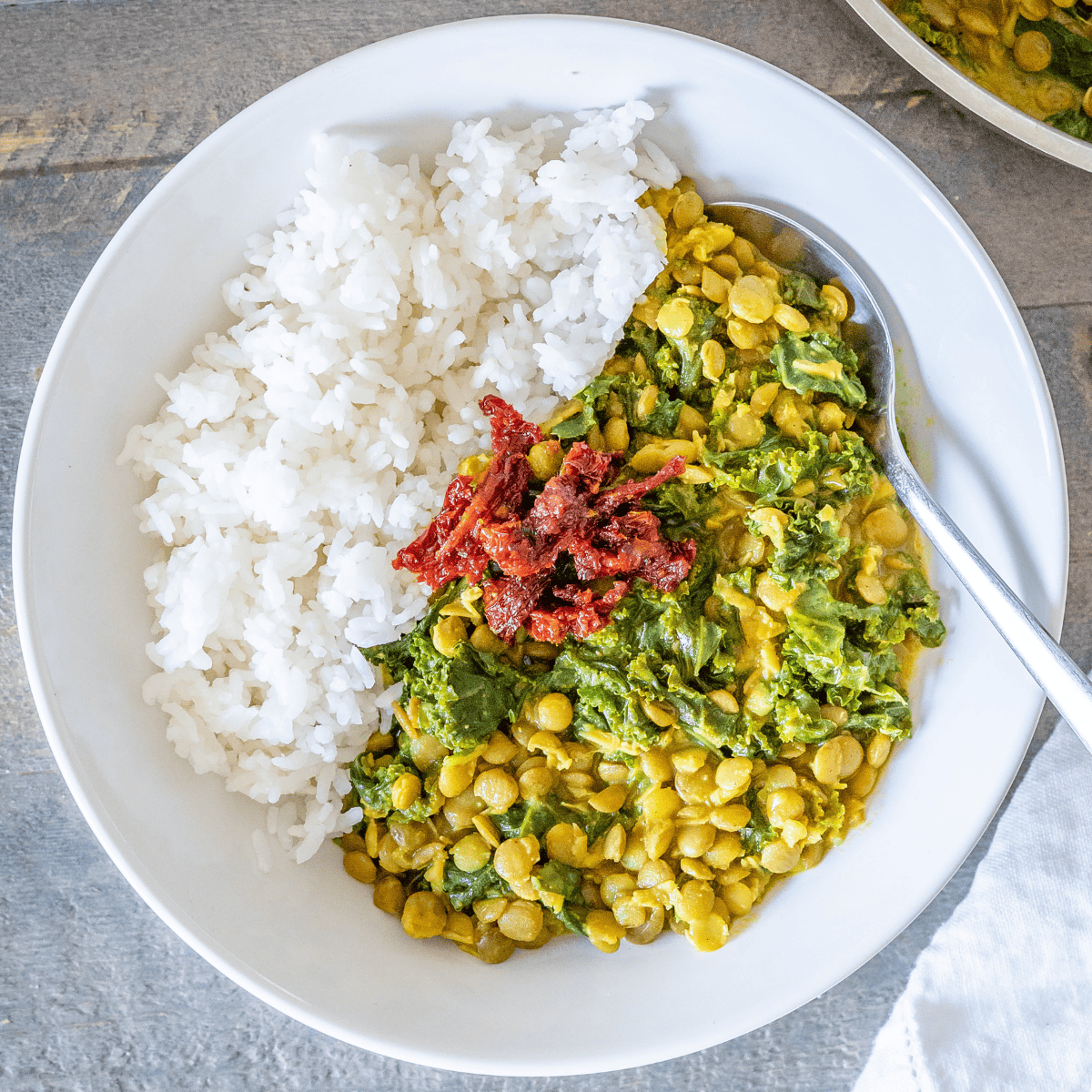 A bowl of kale lentil curry with rice and topped with sun-dried tomatoes.