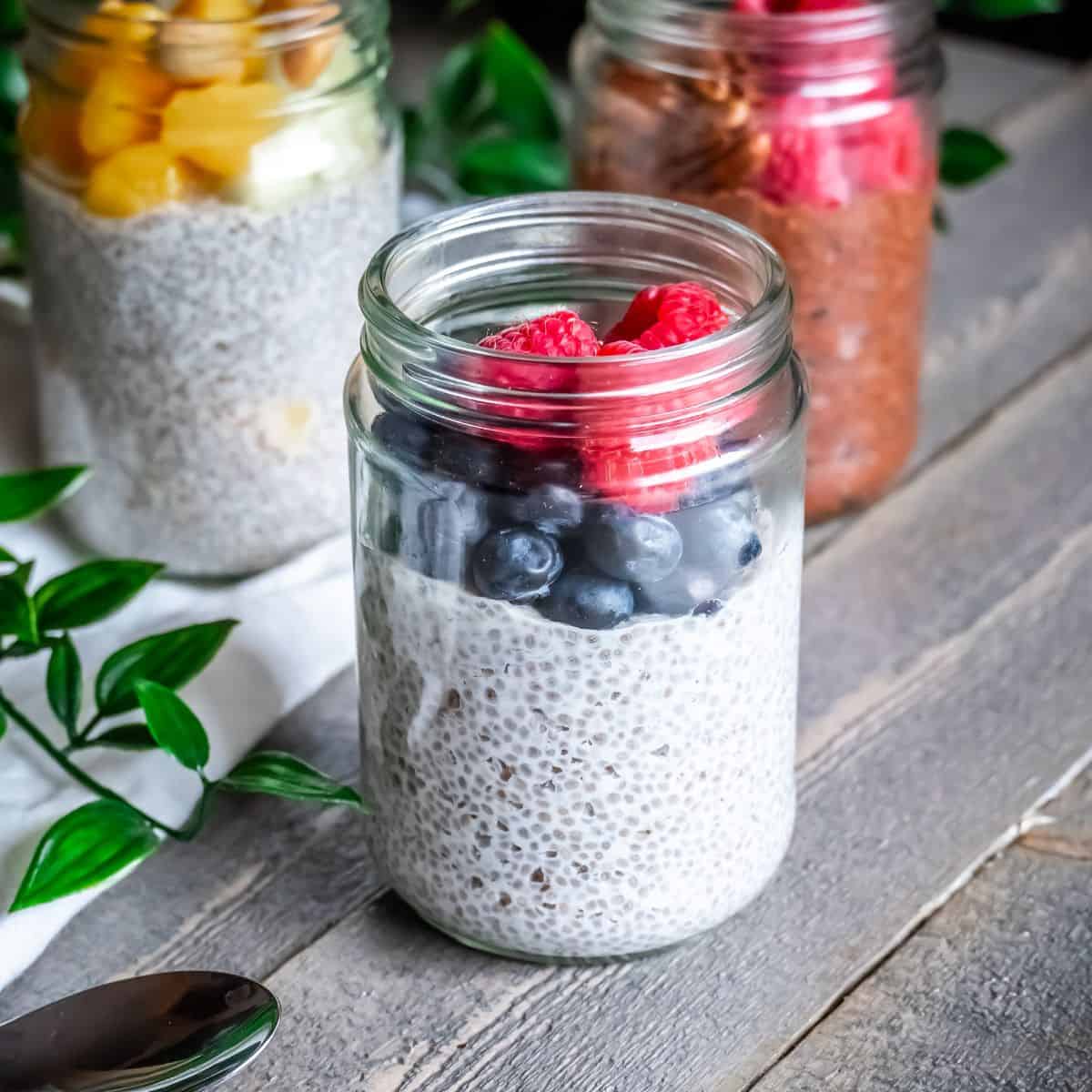 A glass jar with paleo chia seed pudding topped with fresh blueberries and raspberries.