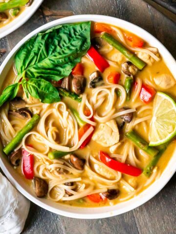 A bowl of thai chicken soup with a creamy coconut milk broth, noodles, and vegetables.