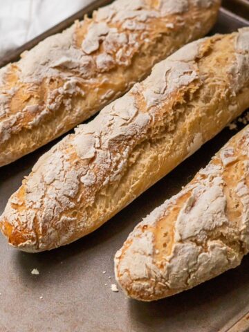 Three freshly baked gluten-free french baguettes on a baking sheet.