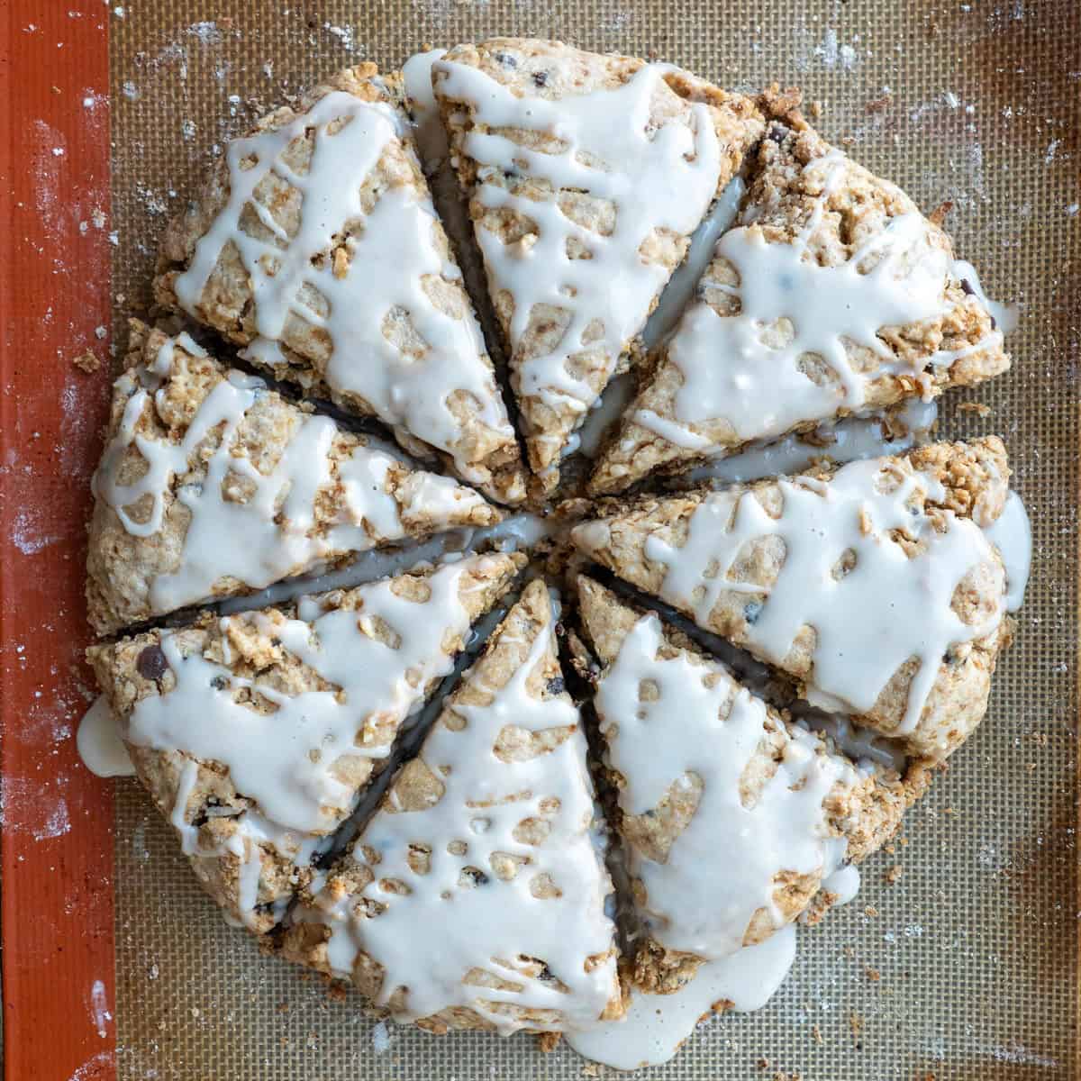 Eight freshly baked gluten-free scones with a maple glaze on a baking sheet.