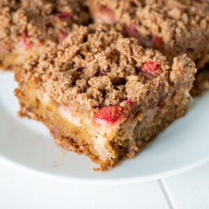 A close up of a piece of gluten-free strawberry rhubarb coffee cake to show the cake, fruit, and crumble layers.