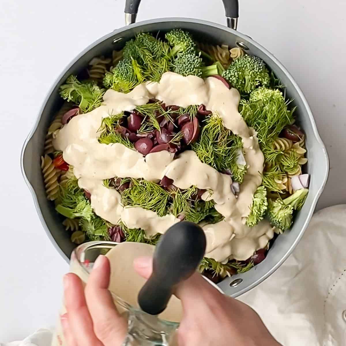 Pouring lemon and garlic tahini dressing over a large bowl of freshly chopped vegetables.
