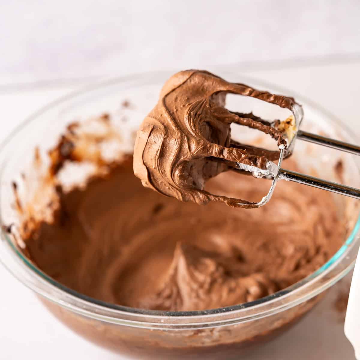 Two electric beaters coated in a thick and creamy vegan and dairy-free chocolate frosting.