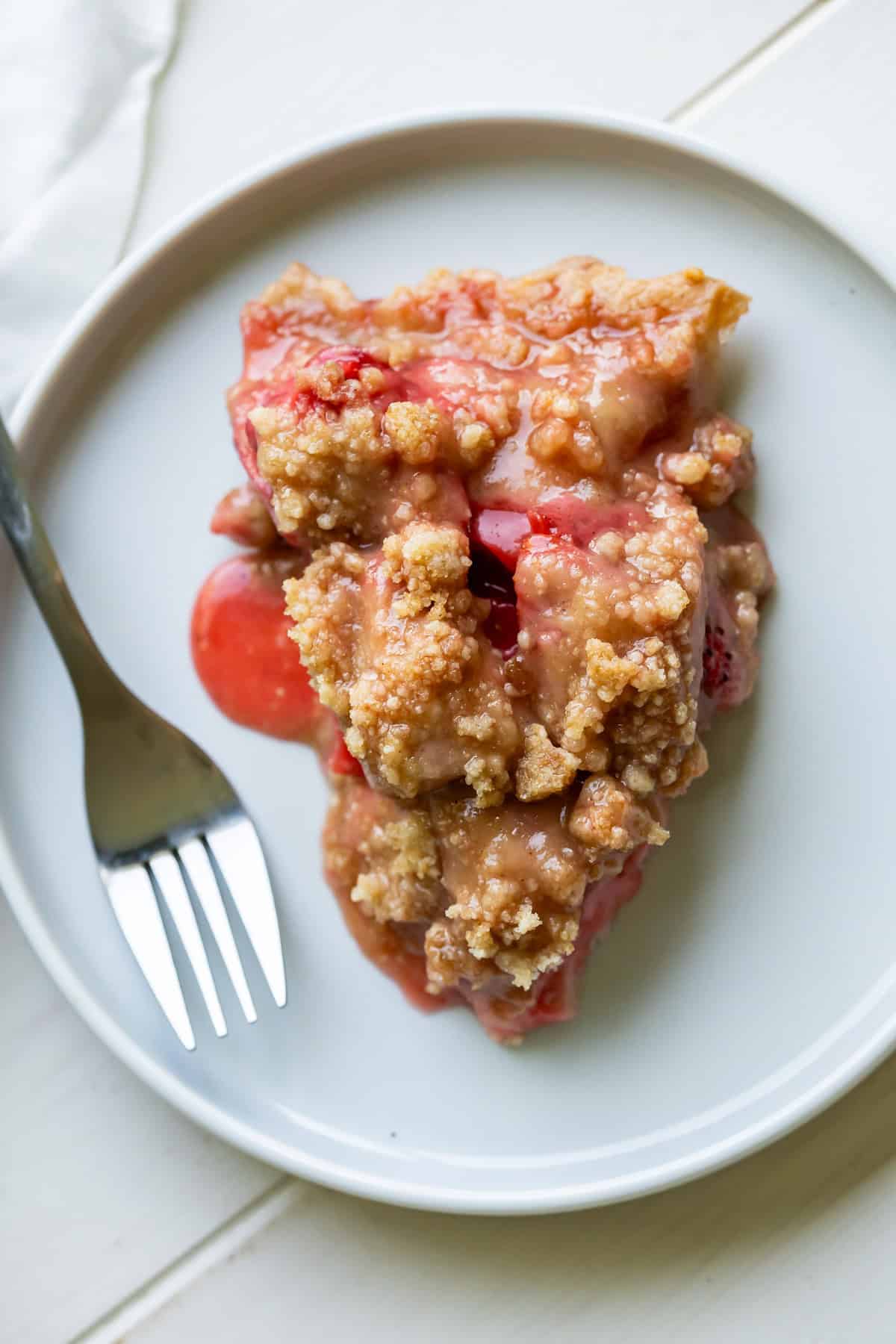 A slice of baked strawberry crumble pie served on a plate.
