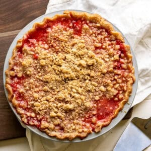 A baked strawberry pie with crumble topping and a bright red strawberry filling.