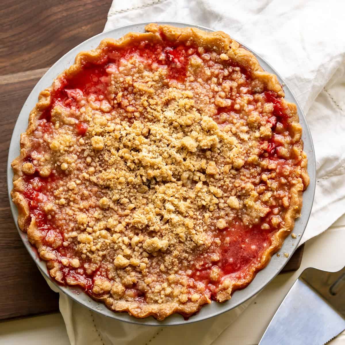 A baked strawberry pie with crumble topping and a bright red strawberry filling.