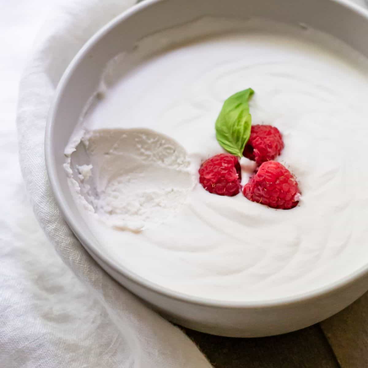 A serving bowl of soft dairy free whipped cream decorated with a mint leaf and three raspberries.