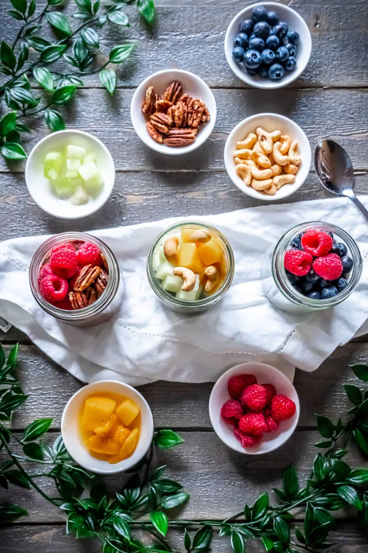 Three chia pudding jars topped with a variety of fresh fruit and nuts.