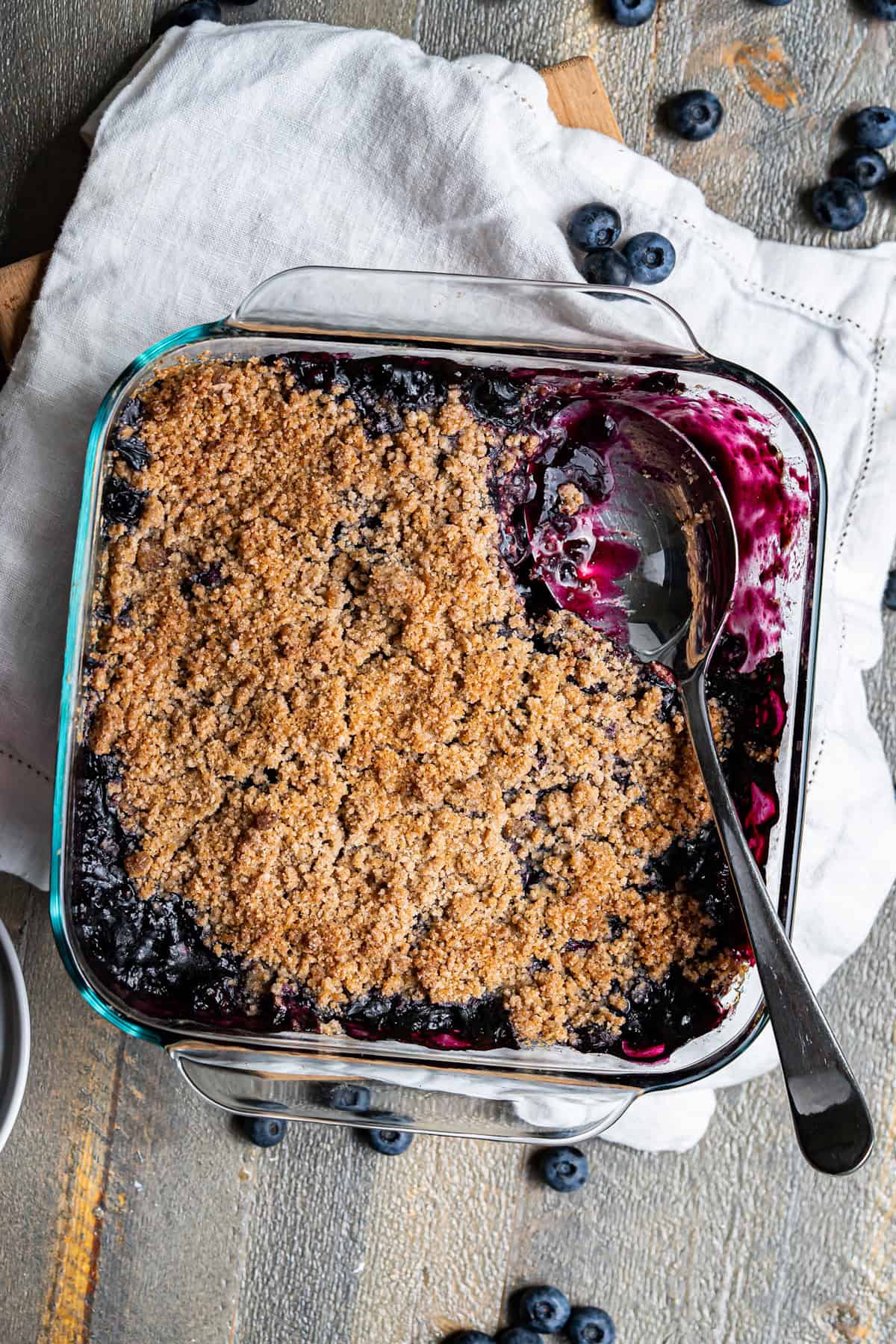 A square glass baking dish filled with blueberry crumble.
