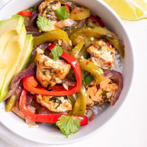A healthy baked chicken fajitas served in a bowl over rice.